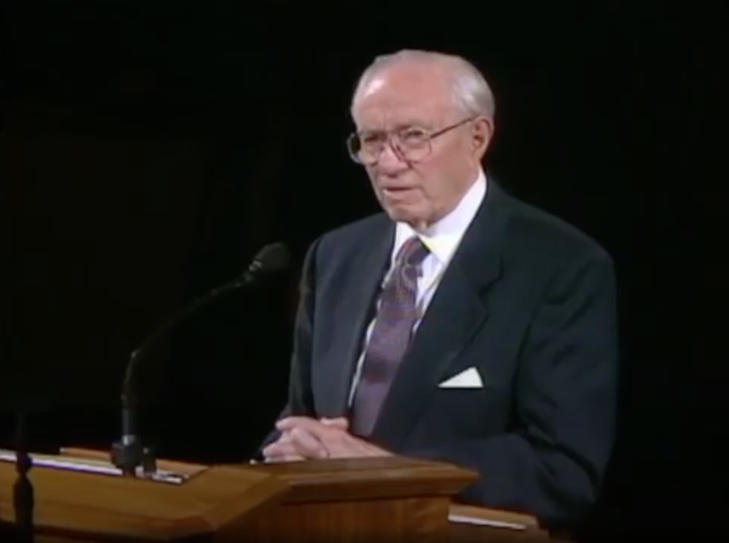A capture of a video broadcast showing President Gordon B Hinckley at the pulpit in front of a black background reading the Family Proclamation for the first time as part of his message at the General Relief Society Meeting held September 23, 1995, in Salt Lake City, Utah.
