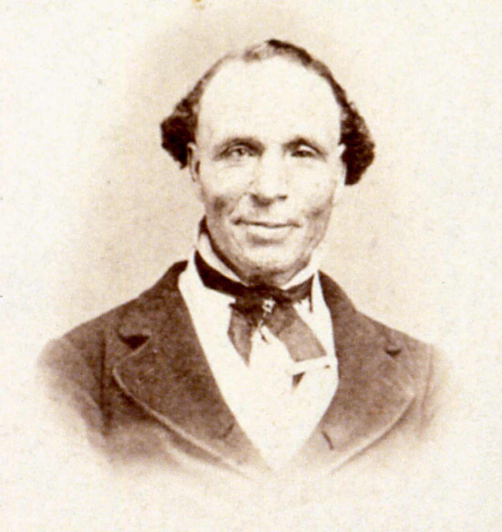 A historical sepia-toned portrait of Elijah Abel. He is wearing a dark suit with a white shirt and a cravat tied neatly at the neck. His hair is short, with a receding hairline. The background is faded.