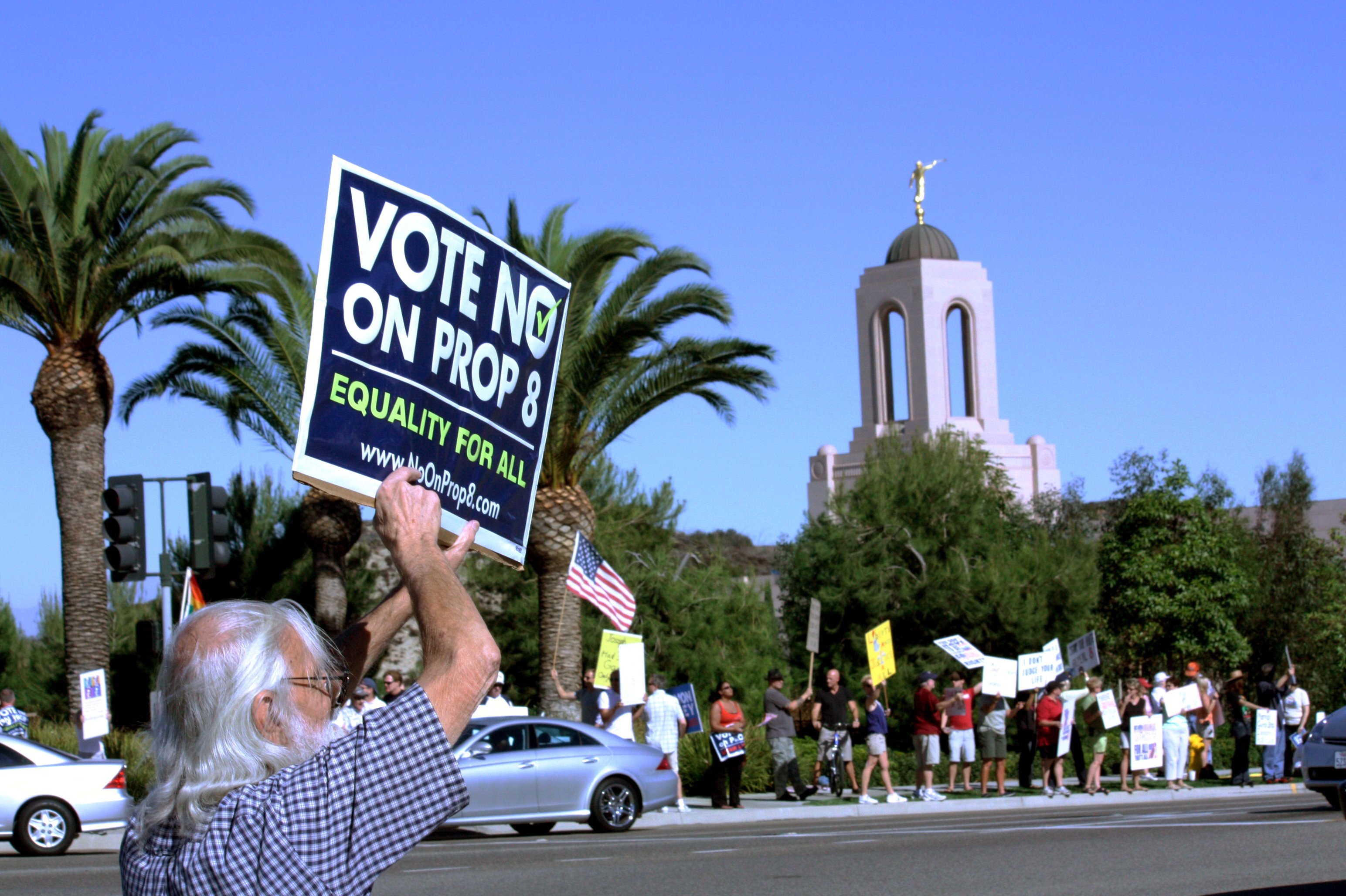 A man with gray hair holds a sign that says 'vote no on prop 8 - equality for all' outside of the LDS Newport temple in California.