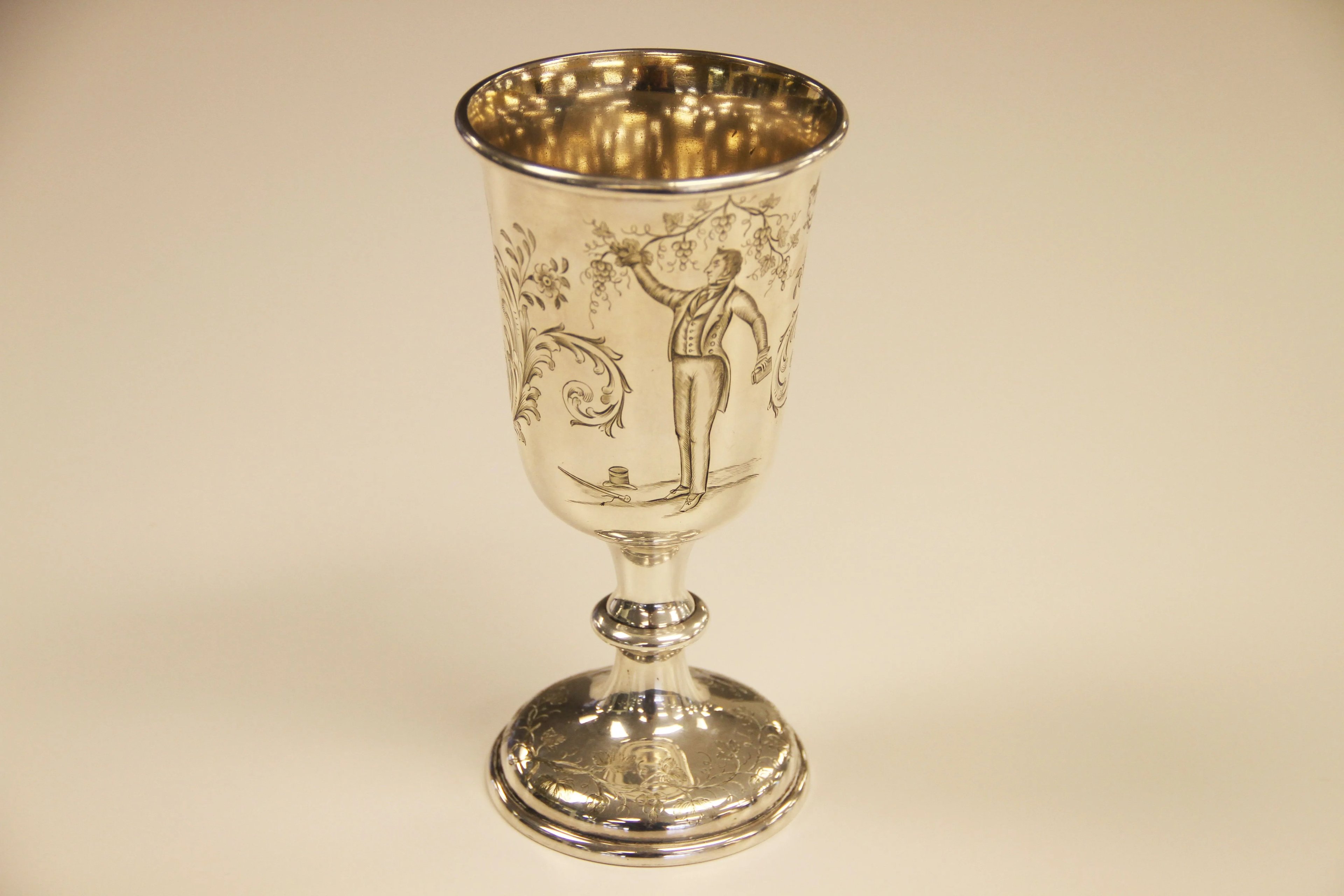 An image of a silver goblet from 1847 against a plain background, used in Latter-day Saint or Mormon sacrament services, with an engraved image of Joseph Smith among grapevines.