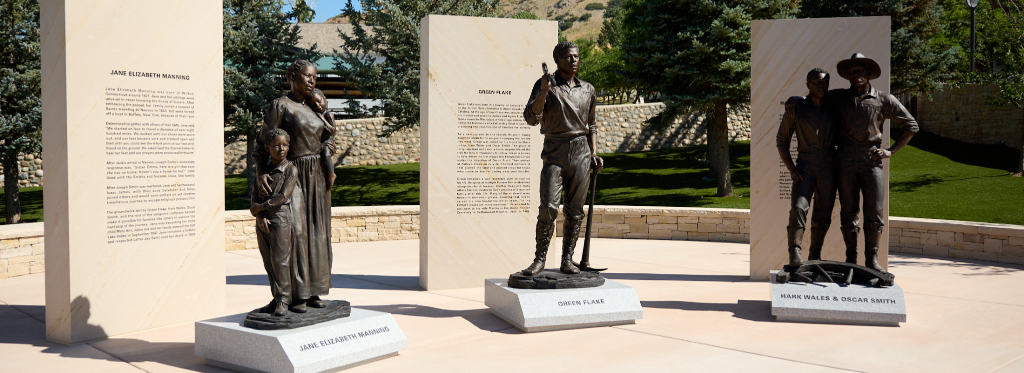 Statues at the "Pioneers of 1847: Monument to Black Pioneers" in This Is the Place Heritage Park, Salt Lake City, Utah. The monument features bronze sculptures of Jane Elizabeth Manning James, Green Flake, and brothers Hark Wales and Oscar Smith, each accompanied by engraved stone panels sharing their stories. The memorial honors the contributions of early Black Latter-day Saint pioneers in the westward migration and settlement of Utah.