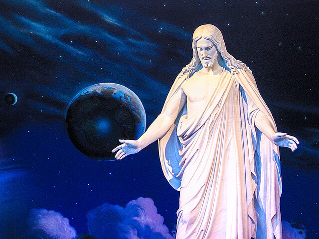 A white marble statue depicts Jesus Christ with outstretched arms. Behind the statue is a celestial-themed mural featuring a deep blue starry sky with planets and clouds.