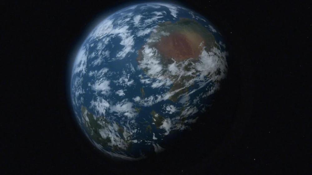 A view of the fictional planet Kobol from space, as depicted in Battlestar Galactica. The planet appears Earth-like with blue oceans, white cloud cover, and large landmasses, including a prominent reddish-brown region. Set against the black backdrop of space.