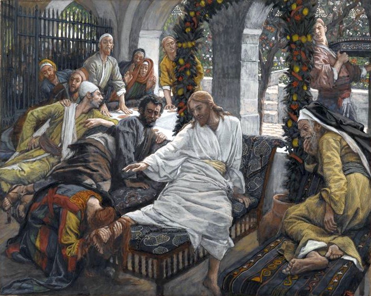 A painting by James Tissot titled The Ointment of the Magdalene shows Jesus seated at a gathering while Mary Magdalene kneels at His feet, anointing them with ointment and wiping them with her hair. Jesus, dressed in white, gestures gently toward her. Onlookers react with a mix of curiosity, disapproval, and surprise. The setting is a stone courtyard decorated with garlands of fruit, and figures crowd around, highlighting the tension and intimacy of the moment.
