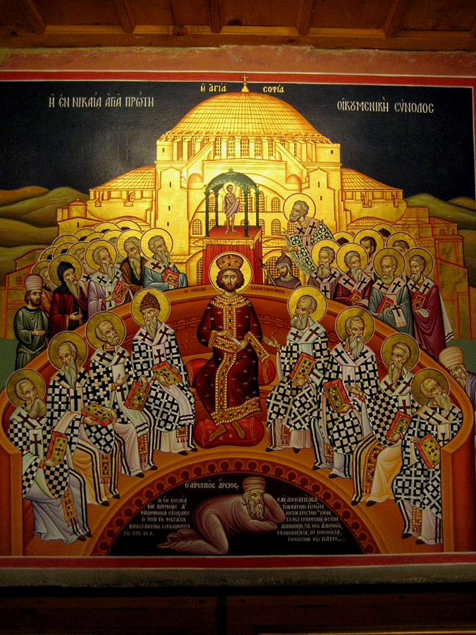 An icon-style painting of the First Council of Nicaea. At the center sits Emperor Constantine in royal robes and crown, surrounded by bishops in white and black checkered vestments holding books of scripture. Behind them rises the domed church of Hagia Sophia. At the bottom of the image, a figure representing Arius lies humbled. The Greek inscription identifies the scene as the First Ecumenical Council of Nicaea.