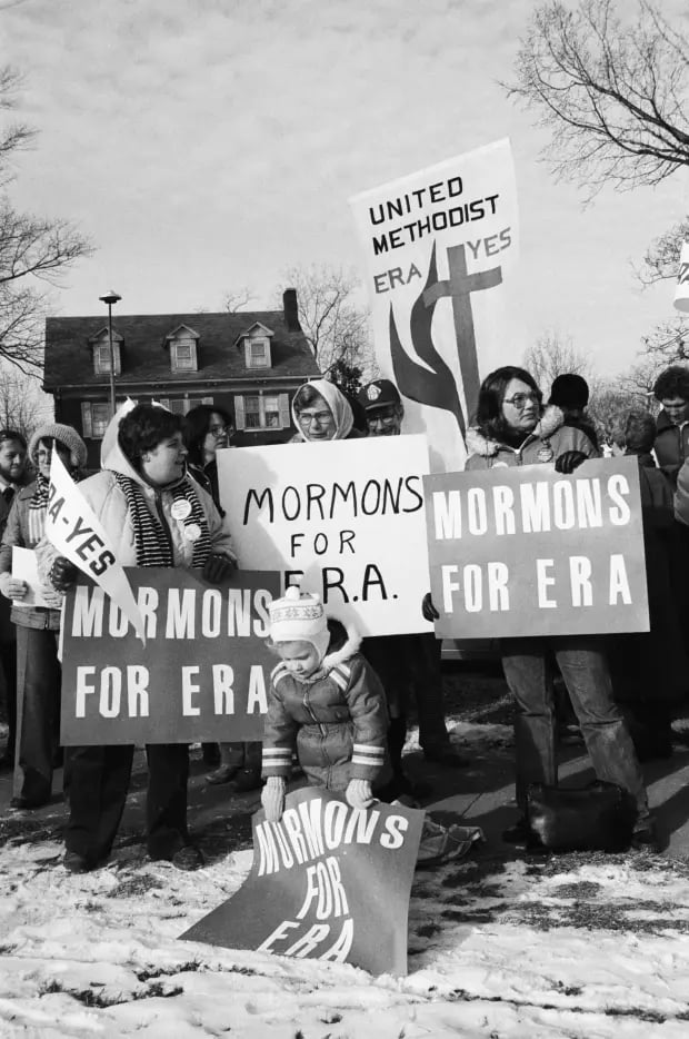 A black and white image from 1981 of a small crowd with signs that read 'Mormons for ERA' standing in the snow, demonstrating on behalf of the Equal Rights ammendment.