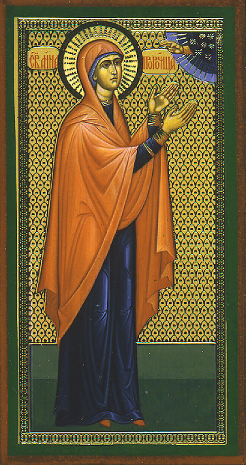 A traditional Orthodox icon depicting Anna the Prophetess. She is shown wearing a dark blue robe with an orange mantle, her hands raised in prayer. A golden halo surrounds her head, signifying her holiness. The background features an intricate golden pattern, and in the upper right corner, a small portion of a divine figure is visible, symbolizing her recognition of the Christ child.