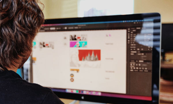 Beeld van over iemands schouder van een man die op een computer aan websiteafbeeldingen werkt.