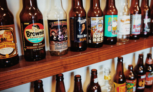 Wooden wall shelves holding rows of various gourmet root beer bottles.