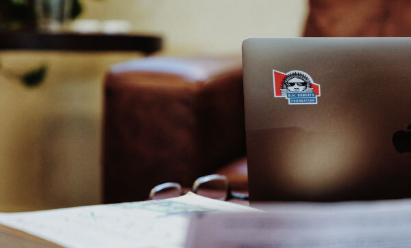 Opengeklapte laptop toont een sticker met het logo van de B. H. Roberts Foundation, met daarop een Nauvoo Sunstone met zonnebril.