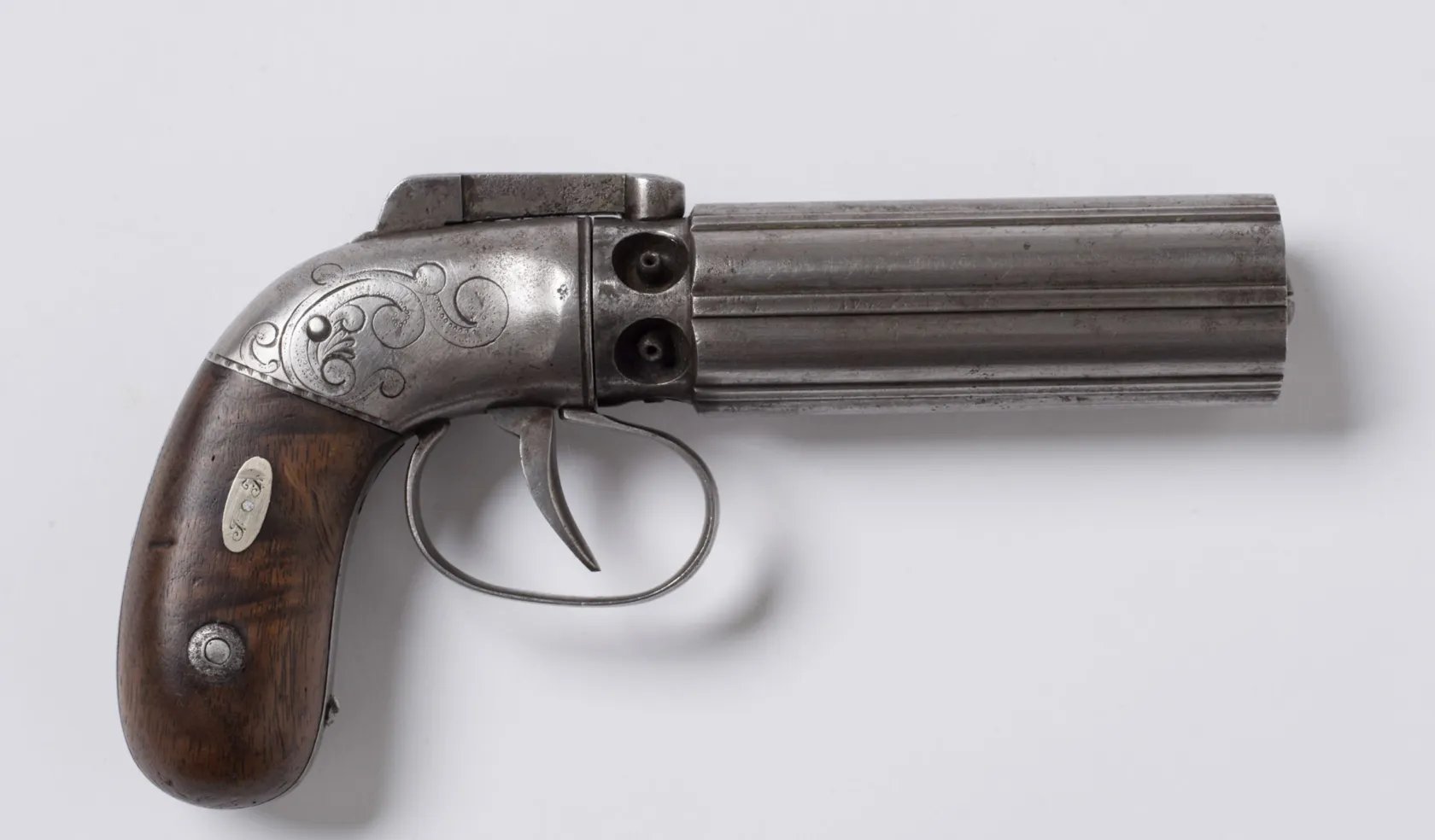 Afbeelding van een gegraveerd zilveren peperbuspistool met een houten handvat dat door Joseph Smith werd gebruikt toen hij werd aangevallen in de gevangenis van Carthage, Illinois, op een witte achtergrond.